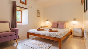 A bedroom with a bed, bedside tables, a chair, a window, and a picture on the wall.