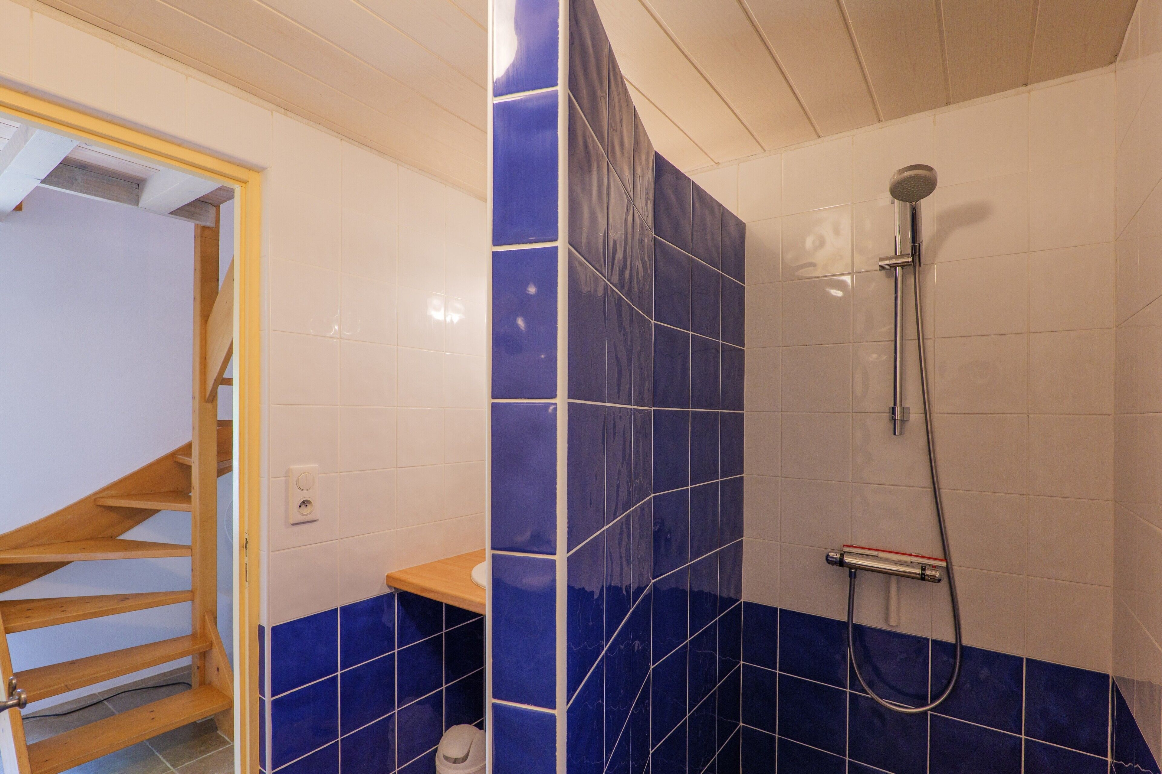 A bathroom with a shower, a wooden shelf, and a tiled wall.