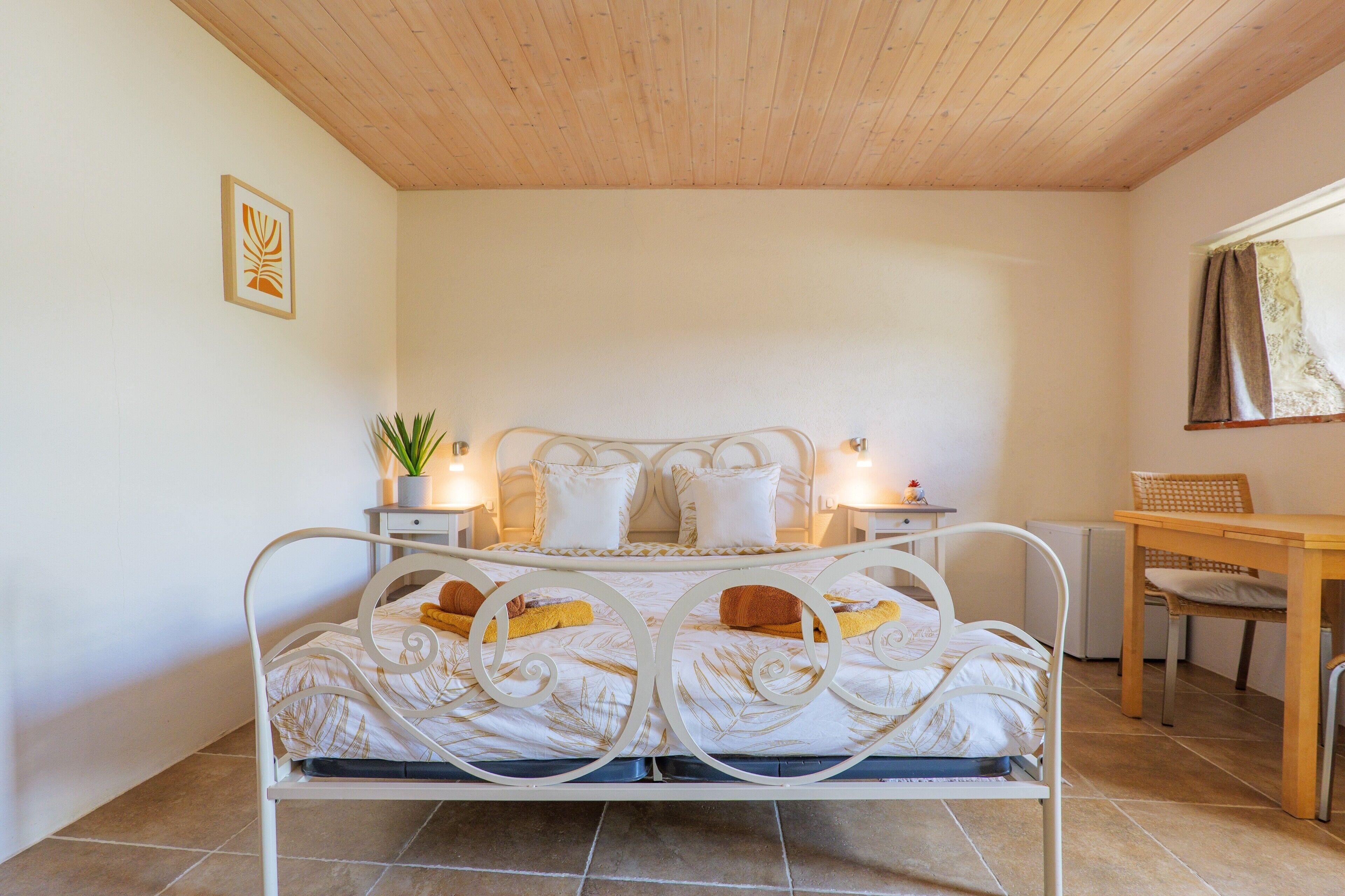 A bedroom with a bed, bedside tables, a chair, a small table, and a window with curtains.