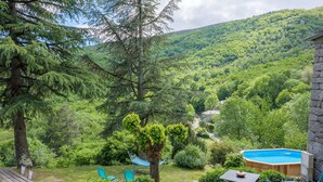 Un patio de piedra con jacuzzi, una mesa y sillas, rodeado de abundante follaje y montañas al fondo.