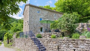Un edificio de piedra con una escalera que conduce a una puerta, rodeado de follaje y un muro de piedra.