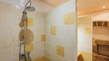 Ducha con cabezal de ducha de mano y grifo empotrado en la pared, paredes con azulejos de diseño variado, combinando baldosas cuadradas y rectangulares, y techo de madera.