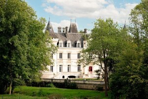 A large, historic building with multiple towers and a central entrance, surrounded by lush greenery.