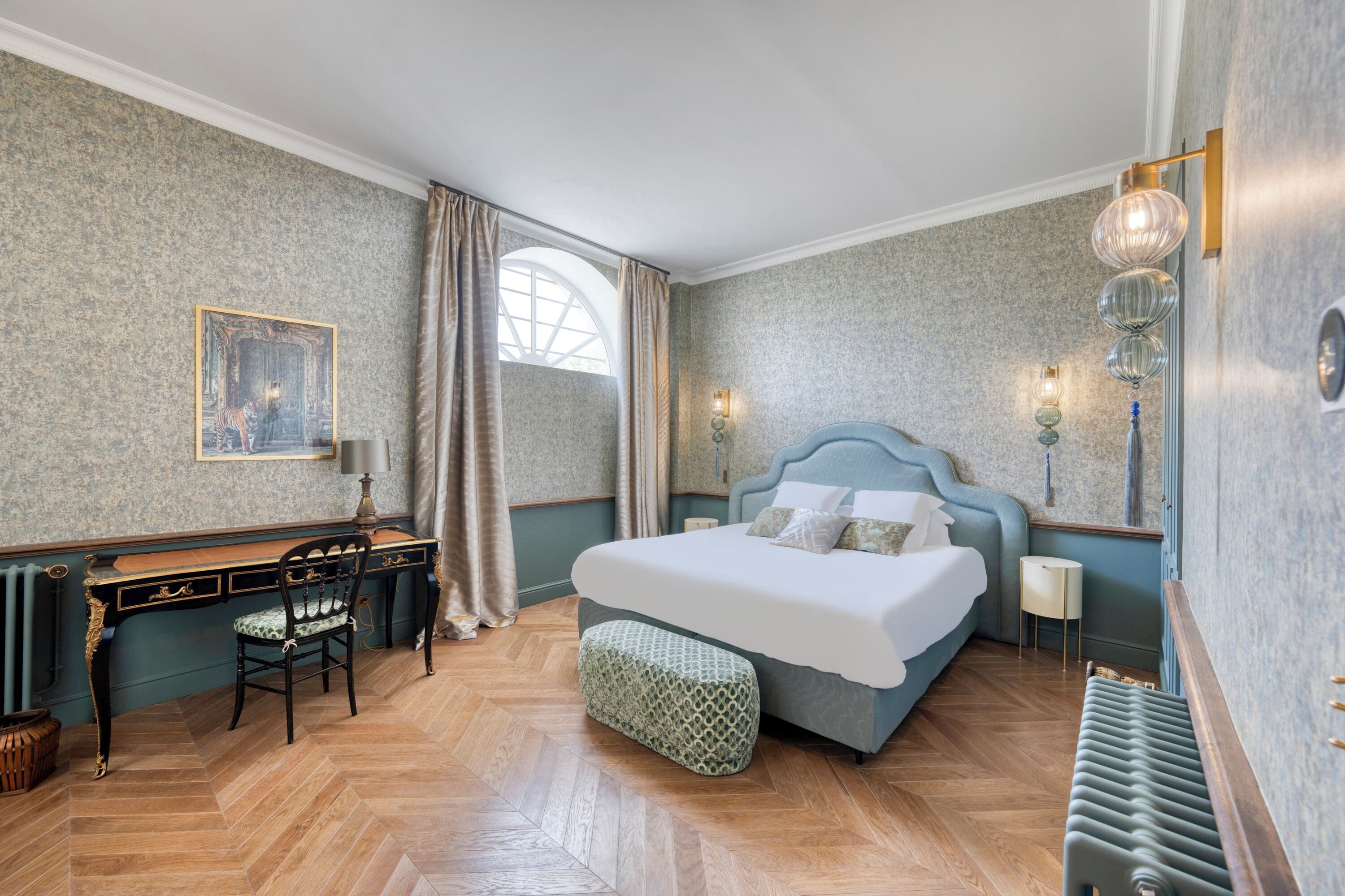A bedroom with a bed, a desk, a chair, a radiator, and a window.