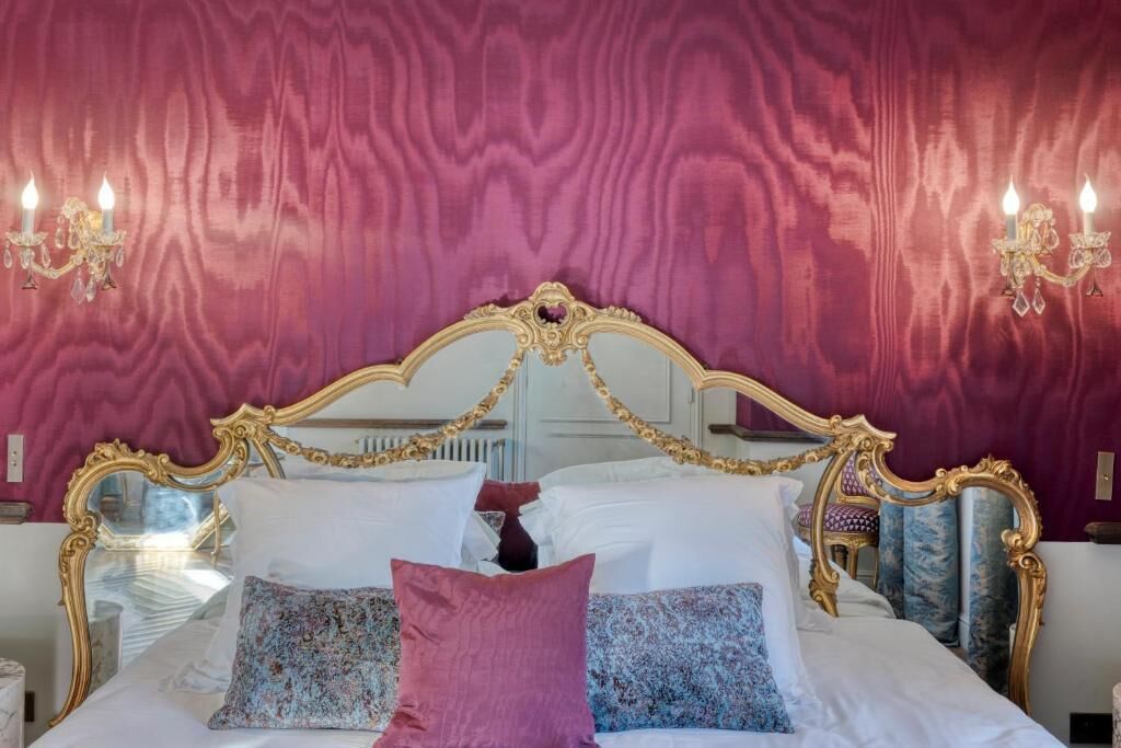 A bed with ornate gold detailing, a mirror, and two wall sconces with candles.
