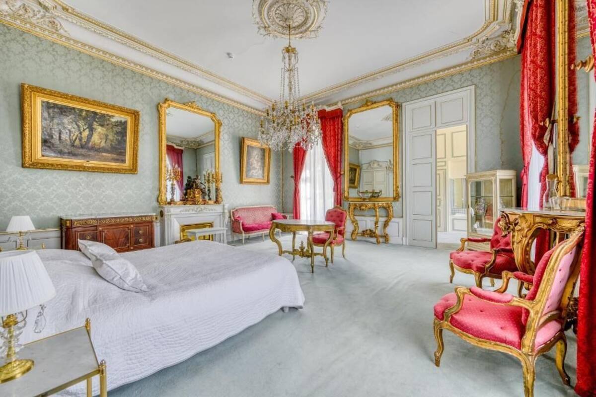 Een luxueuze slaapkamer met een groot bed, een kroonluchter, een open haard en versierde meubels.