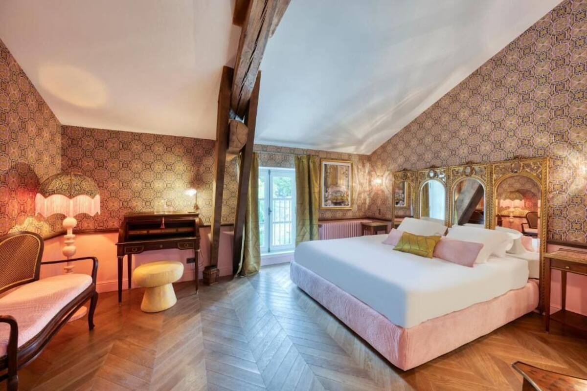 Hotelkamer met een groot bed, een bureau met lamp, een stoel en een raam met gordijnen.