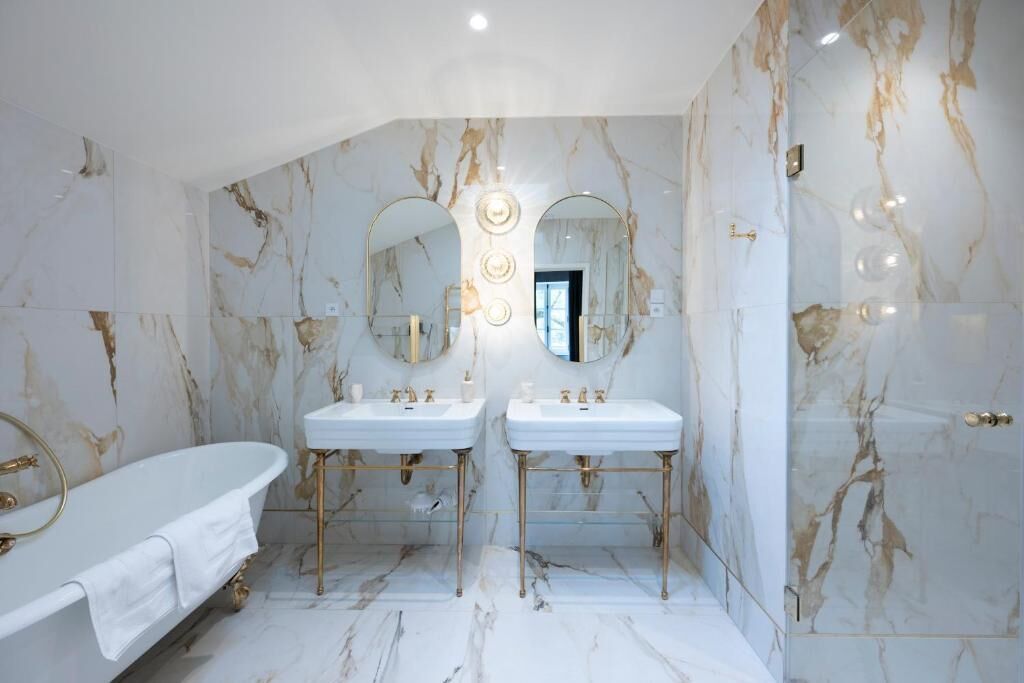 A bathroom with two sinks, a bathtub, and marble walls.