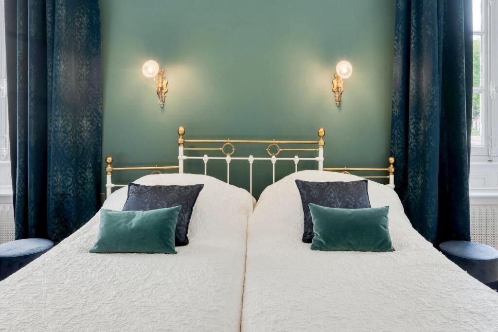 A double bed with a white and green color scheme, two wall-mounted lights, and a green wall.