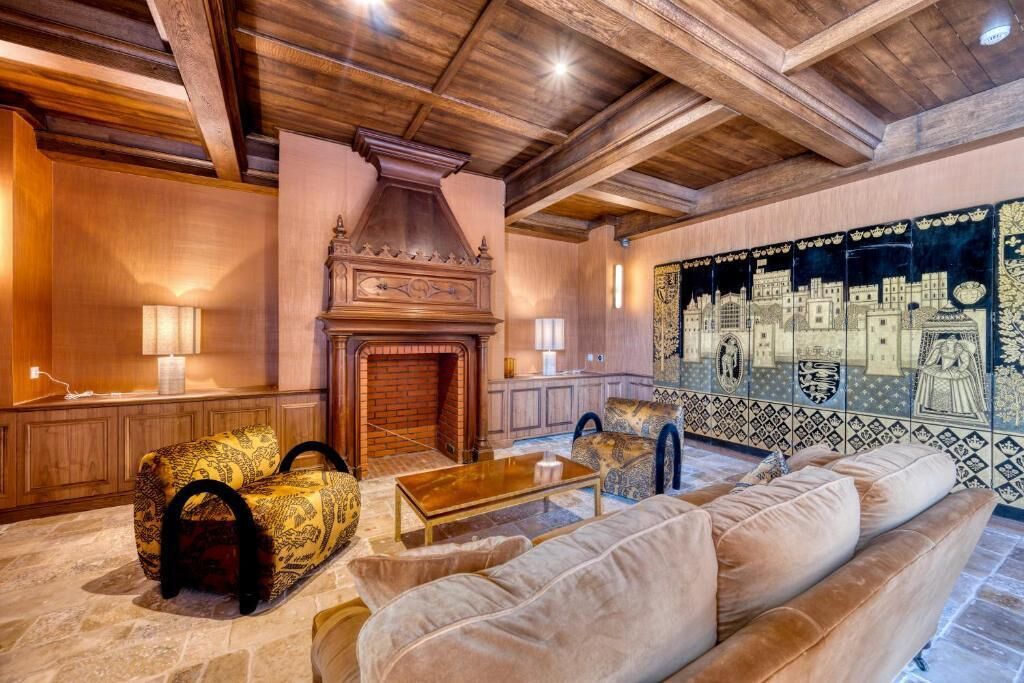 A room with a fireplace, a sofa, a patterned armchair, and a tiled wall with a cityscape mural.