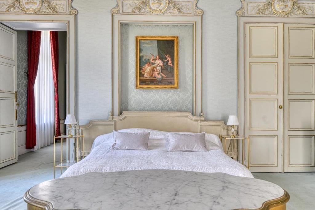 A bedroom with a large bed, a painting above the bed, and a wardrobe with a mirror.