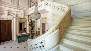 A grand staircase with ornate white railings and a chandelier. - Château Optical Center (Nieuil)