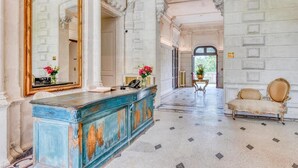 A grand hallway with a blue cabinet, a large mirror, and a classic chair. - Château Optical Center (Nieuil)