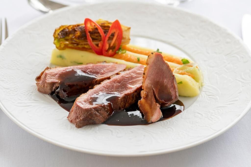 A plate with sliced meat, vegetables, and a sauce.