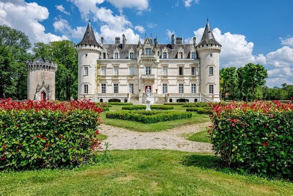 Un castillo grande e histórico, con un patio central, rodeado de jardines cuidados y una torre.