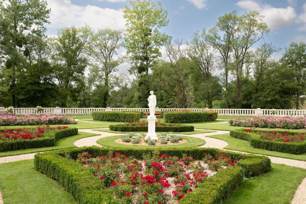 A formal garden with a central statue, manicured hedges, and flowering plants.