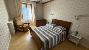 A bedroom with a wooden bed, a chair, a dresser, a nightstand, and a window with curtains. - Country House (Motorcyclists Welcome) 50 m from the Dordogne River (Beaulieu-sur-Dordogne)