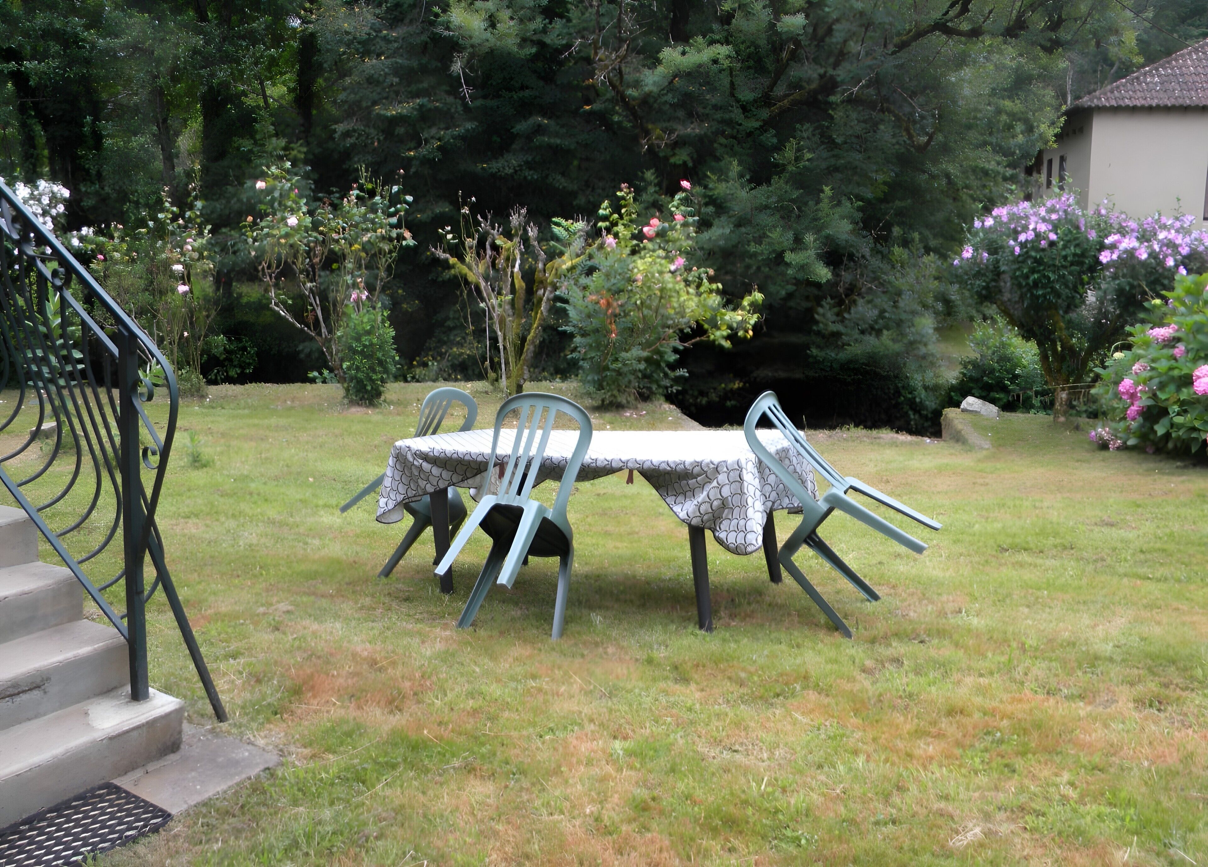 A garden with a table and chairs, surrounded by trees and flowers.