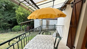 Ein Balkon mit Tisch und Stühlen, einem gelben Sonnenschirm und Blick auf den Garten.