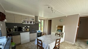 A compact kitchen with modern appliances, a dining table with chairs, and a clock on the wall. - Country House (Motorcyclists Welcome) 50 m from the Dordogne River (Beaulieu-sur-Dordogne)