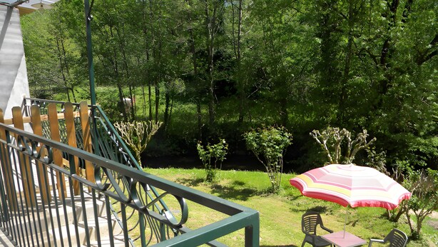 A balcony with a metal railing, a table with chairs, and a colorful umbrella. - Country House (Motorcyclists Welcome) 50 m from the Dordogne River (Beaulieu-sur-Dordogne)
