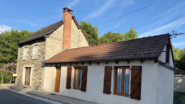 Ein zweistöckiges Steinhaus mit Ziegeldach, Holzhörnern und einem Schornstein.