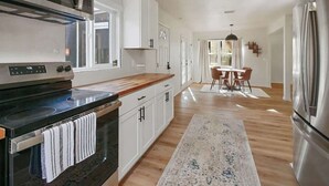 Een moderne keuken met een fornuis, magnetron en koelkast, houten vloer, en een eethoek met stoelen en een tafel.