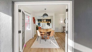 Een open deur die leidt naar een eetgedeelte met een houten tafel en stoelen, een plafondventilator en een hanglamp.