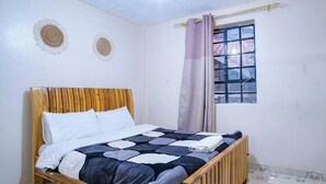Una cama individual con estructura de madera, una colcha estampada y una ventana con cortina.