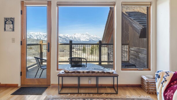 Una cabaña con puerta de madera, un banco, vistas de montañas nevadas y un balcón con una silla.
