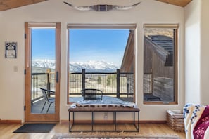 Une cabane avec une porte en bois, un banc, une vue sur des montagnes enneigées et un balcon avec une chaise.