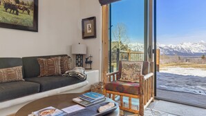Un salón con un sofá, una silla, una mesa de centro y un amplio ventanal con vistas a la montaña.