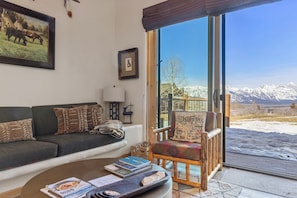 A living room with a sofa, a chair, a coffee table, and a large window offering a mountain view.