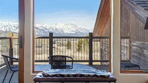 Habitación con vistas a montañas nevadas, una terraza de madera y una mesa con una manta.