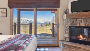 Un dormitorio con cama, chimenea, televisión y balcón con vista a la montaña.