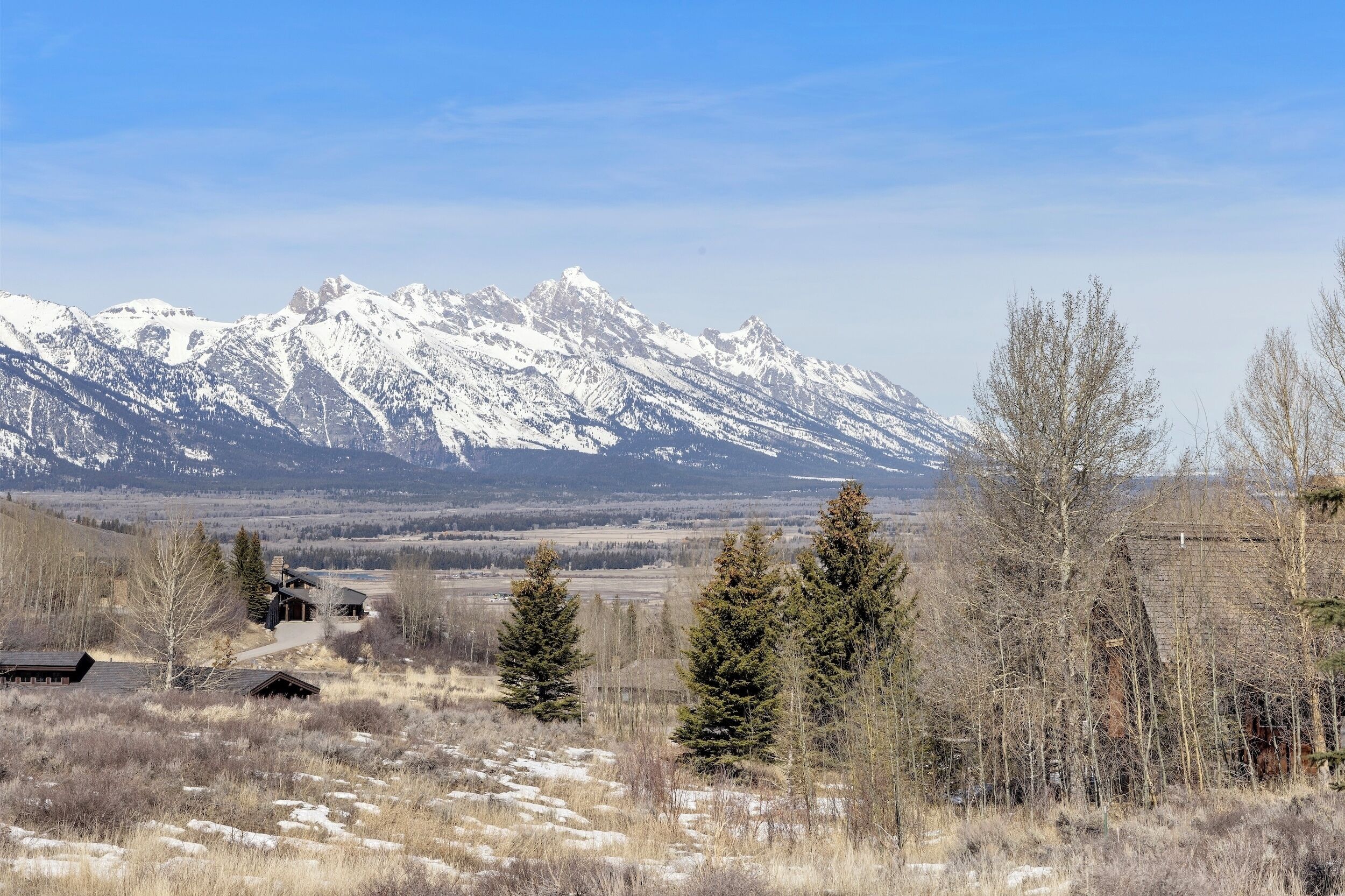 Un paysage montagneux aux sommets enneigés, avec quelques bâtiments et des arbres clairsemés.