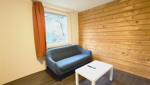 A room with a wooden wall, a window with curtains, a sofa, and a small white table. - Bendorf Hotel by Belvilla Family Suite (Bendorf)