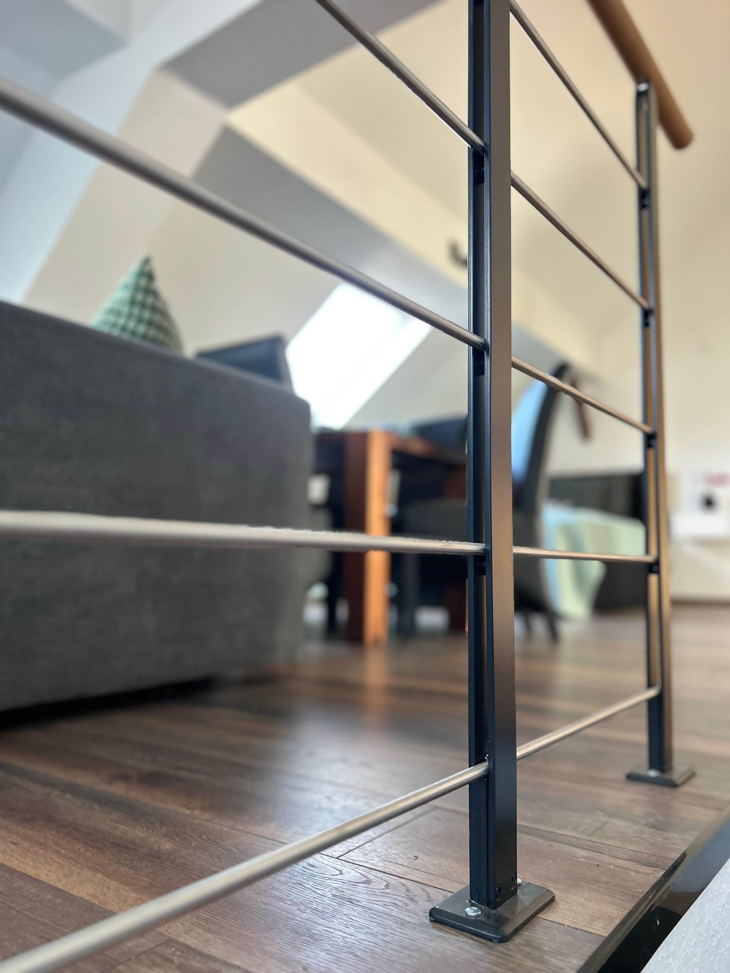A modern interior with a wooden floor, metal railings, and a grey sofa.