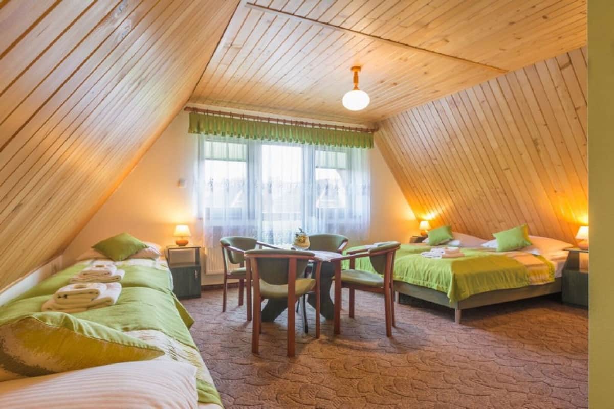 A cozy attic bedroom with two beds, a dining table, and chairs.