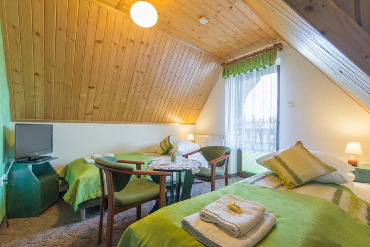 A cozy room with a sloped ceiling, a television, two green beds, a small table, and chairs.