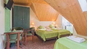A room with a sloped ceiling, two beds with green bedding, a desk with a chair, and a television mounted on the wall. - Dom Wczasowy Na Kamiencu (Białka Tatrzańska)