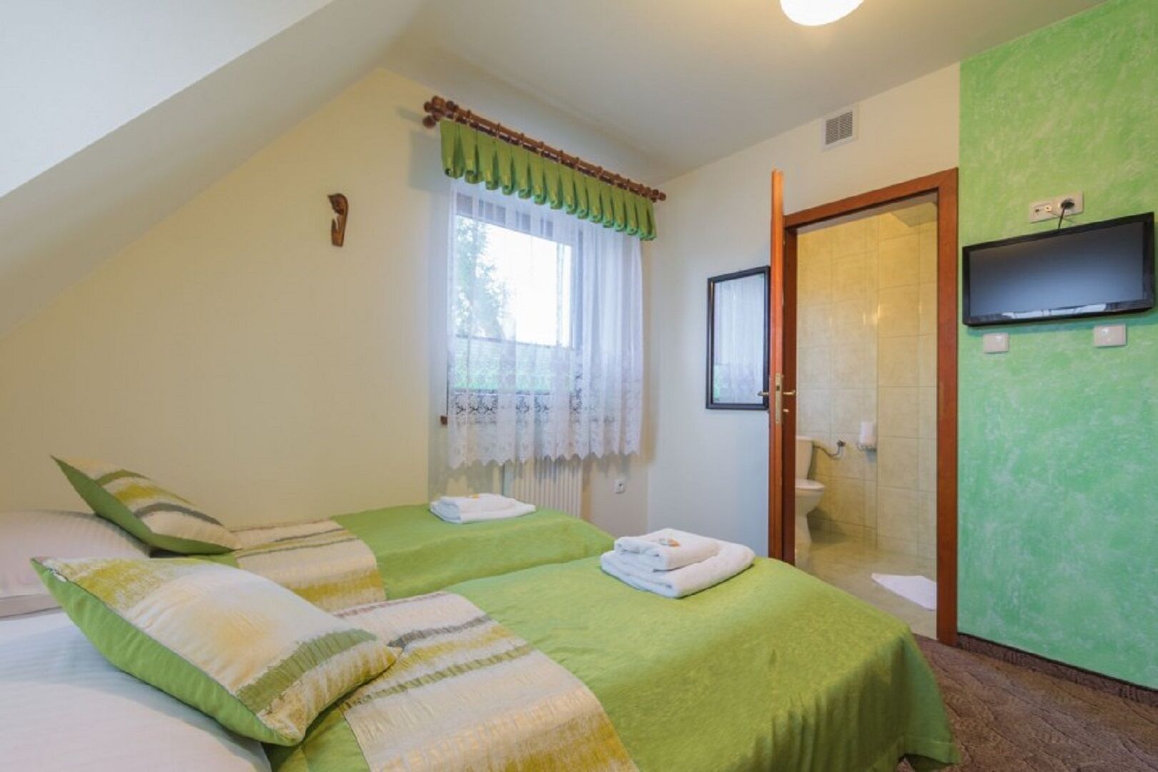 A room with two beds, a window with curtains, a television, and a bathroom.