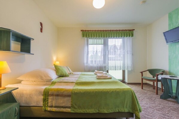 A hotel room with a bed, bedside lamp, chair, and a TV on the wall. - Dom Wczasowy Na Kamiencu (Białka Tatrzańska)