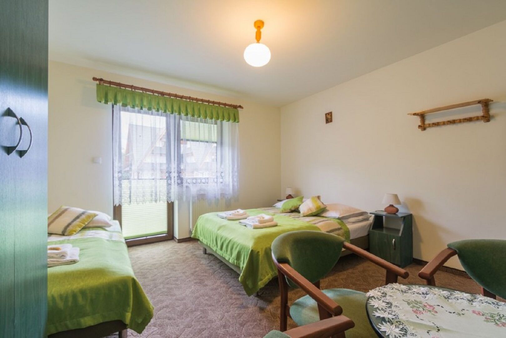 Une chambre avec deux lits, une chaise, une table, une lampe et un luminaire au plafond.