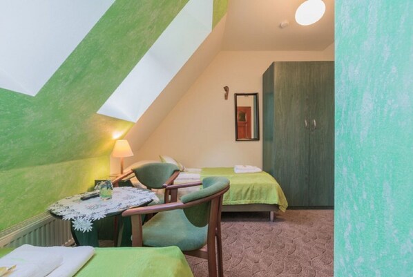 A small, cozy room with a sloped ceiling, a bed, a chair, a table with a lamp, and a wardrobe. - Dom Wczasowy Na Kamiencu (Białka Tatrzańska)