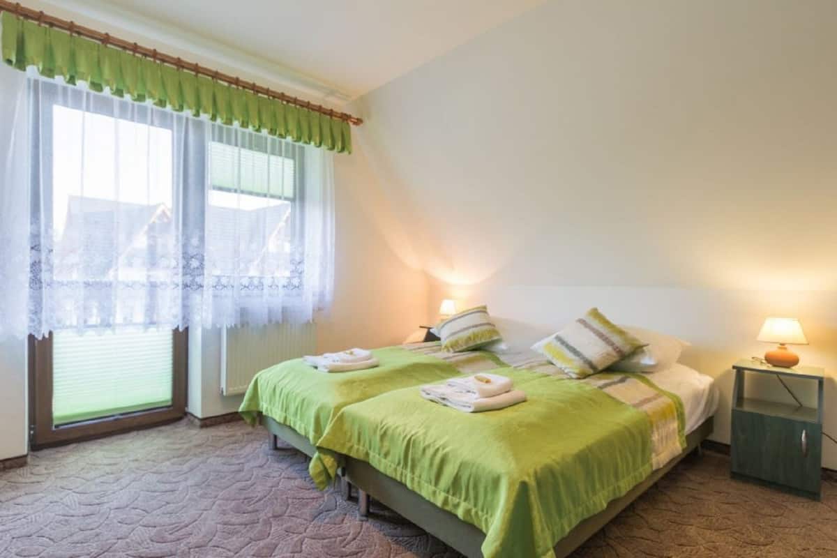 A bedroom with a bed, two bedside tables, a window with curtains, and a lamp on the nightstand.