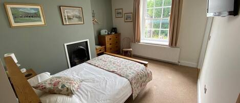 A bedroom with a bed, dresser, chair, and a TV mounted on the wall.