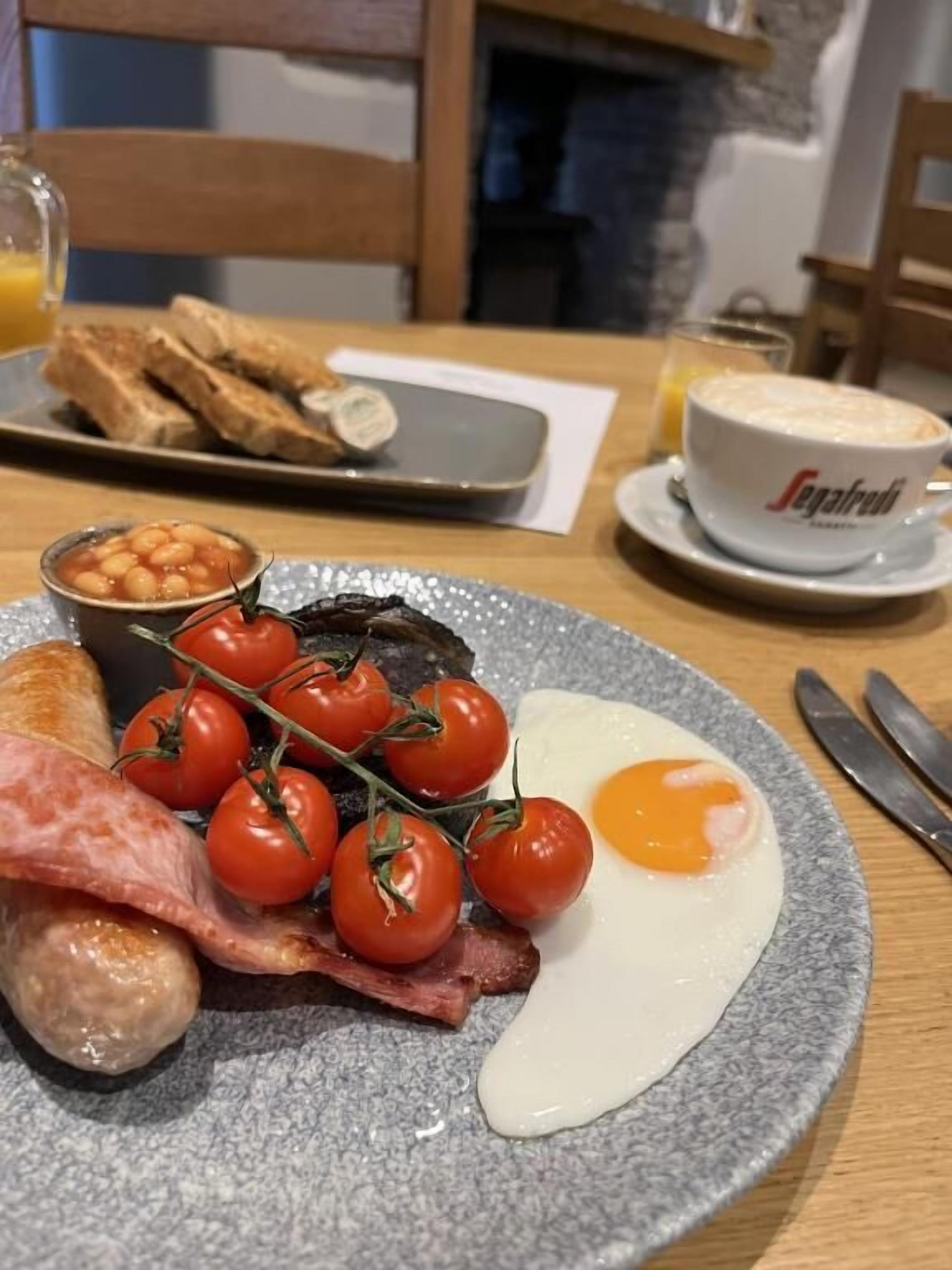 En frukosttallrik med ägg, bacon, tomater, bönor och rostat bröd.
