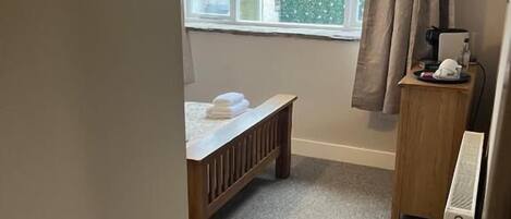 Une chambre à coucher comprenant un lit, une table de chevet, un radiateur, une fenêtre avec des rideaux et une vue sur les bâtiments à l’extérieur.