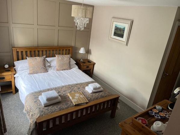 A hotel room with a bed, bedside tables, a nightstand, a wooden bench, a chandelier, a framed picture, and a tray with items. - The Temple Bar Inn (Hereford)